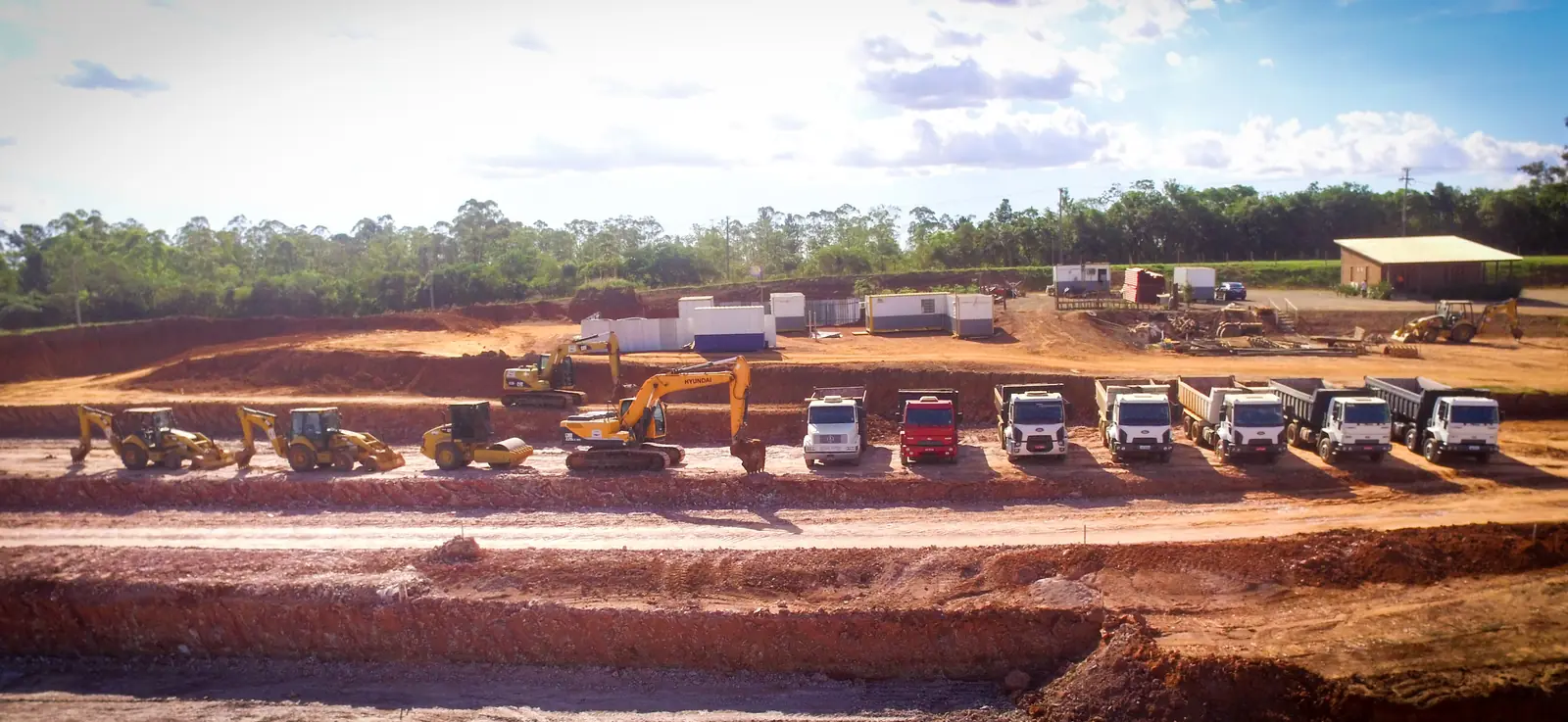 Vista panorâmica de obra de terraplenagem com caminhões e máquinas enfileirados